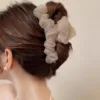 Gros plan de l'arrière de la tête d'une femme aux cheveux bruns coiffés en chignon élégant, ornés d'un chouchou à volants de couleur claire. La personne porte également des boucles d'oreilles en perles et a la Grande Épingle à Cheveux en Maille pour Femmes délicatement glissée dans le chignon.