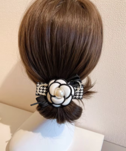 Vue arrière d'une tête de mannequin aux cheveux bruns coiffés en chignon bas, ornée d'une Pince à Cheveux Fleur de Camélia Classique aux accents noirs et blancs et d'une perle.