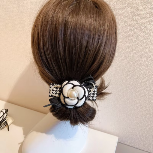 Vue arrière d'une tête de mannequin aux cheveux bruns coiffés en chignon bas, ornée d'une Pince à Cheveux Fleur de Camélia Classique aux accents noirs et blancs et d'une perle.