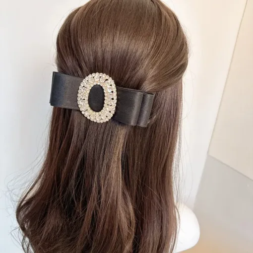 Une personne aux cheveux longs bruns coiffés à moitié relevés porte une grande Pince à Cheveux en Cristal Biscuit noire ornée d'un ornement en cristal de forme ovale.