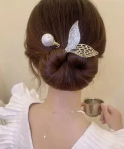 Une femme avec un chignon soigneusement coiffé à l'aide du Rouleau de bandeau en forme de beignet pour chignon, orné d'un accessoire pour cheveux en perles et feuilles, portant un haut blanc à manches à volants, tient une petite tasse dans sa main droite.