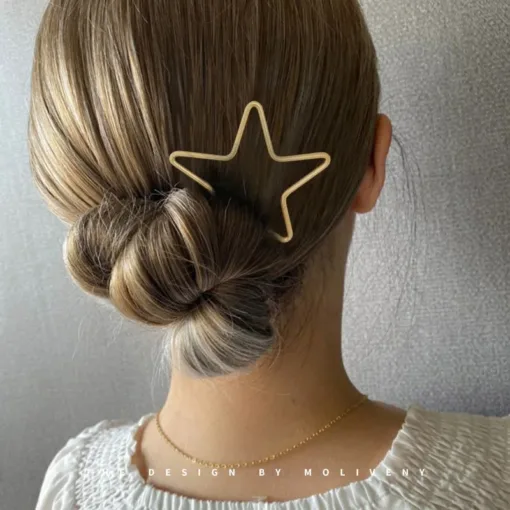 Une personne aux cheveux blonds coiffés en chignon bas porte le Bâton à cheveux en métal en forme d'étoile simple. Elle est vêtue d'un haut blanc avec un tissu texturé.