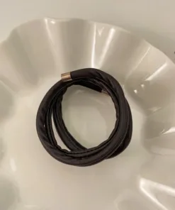 Un bracelet en cuir noir spiralé Chouchous en cuir INS Temperament avec un fermoir en métal repose sur une plaque blanche décorative, ajoutant un élément d'élégance à la monture.