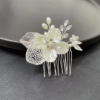 Une Peigne à cheveux en alliage d'or et brun, présentant des motifs floraux et de feuilles blancs ornés de perles et d'accents de cristal, placée sur une surface sombre.