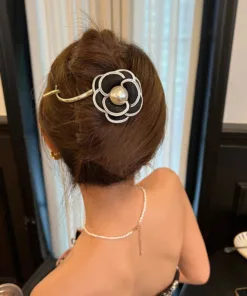 Une personne, les cheveux relevés et ornés d'une Pince à cheveux camélias en métal pour femmes, regarde vers l'extérieur. Elle porte une tenue bustier et un collier délicat.