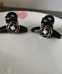 Deux « Pinces à Cheveux Vintage pour Femmes » noires aux motifs en forme de rose avec des accents de perles se détachent sur une surface blanche, complétée par un subtil cœur rouge en arrière-plan.