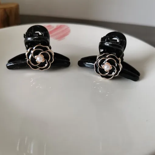 Deux « Pinces à Cheveux Vintage pour Femmes » noires aux motifs en forme de rose avec des accents de perles se détachent sur une surface blanche, complétée par un subtil cœur rouge en arrière-plan.