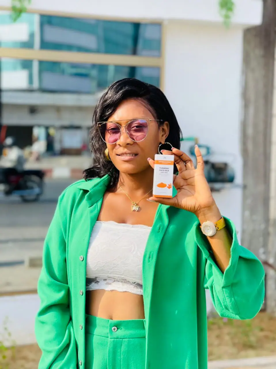 Une personne portant une tenue verte tient une petite bouteille à l'extérieur.