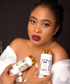 Une femme en robe blanche tient avec assurance deux flacons étiquetés "PILULES BIO ULTIMES + VITAMINE C" et "COLLAGÈNE (le set le plus éclairant)" avec des couvercles dorés, posant sur un fond sombre.