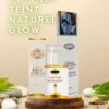 Trois produits Coffret Teint Naturel Glow Belle Nubian - le sérum pour le visage, le savon jeunesse au miel d'abeille et le lait corporel au caramel - sont disposés sur un support en bois avec des pierres et des feuilles vertes, mettant en valeur leur élégance naturelle.