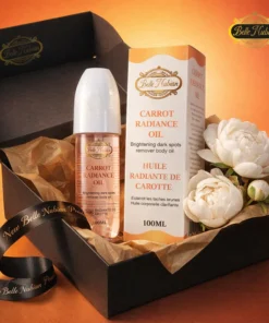 Un coffret noir contient le NOUVEAU Huile éclat à la carotte (100ml) avec son emballage, un ruban et deux fleurs blanches disposées sur du papier de soie brun.