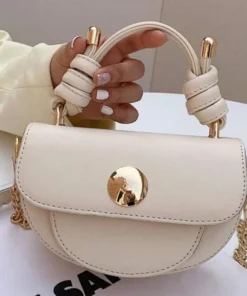 Cream mini handbag with a knotted wrapped ivory handle and gold circular clasp on a white table, held by a hand with white manicured nails.