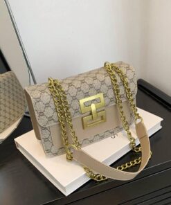 Beige monogram handbag with a gold chain strap and a square gold clasp, resting on a white book surface.