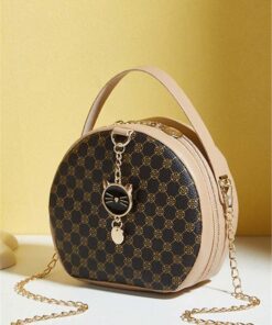 Round designer handbag with beige trim, gold chain strap, and a cat charm on a yellow background.