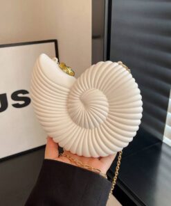 White ribbed shell handbag with a gold chain being held by a person wearing a black sleeve, in an indoor setting.